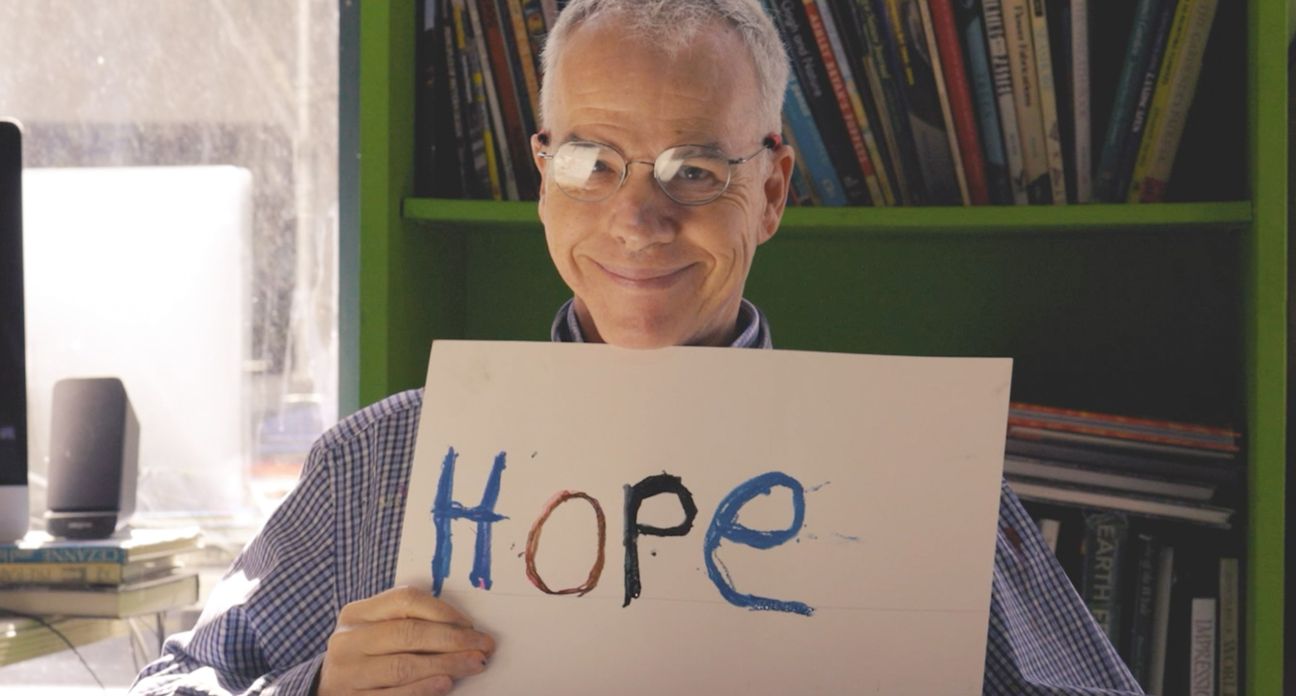 A man wearing glasses holding a piece of paper with the word "HOPE" painted on it.