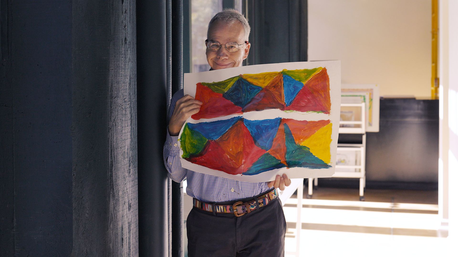 Mickey Daly smiling and holding a piece of his artwork featuring colorful triangles.